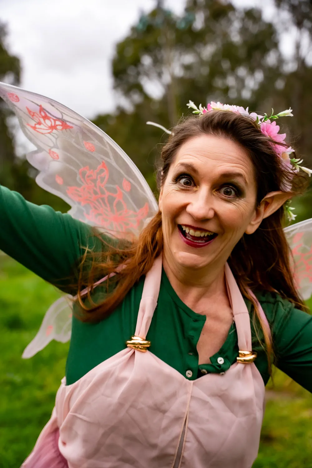 Rama Nicholas in costume as Thistle, grinning wide-eyed with arms flung out.