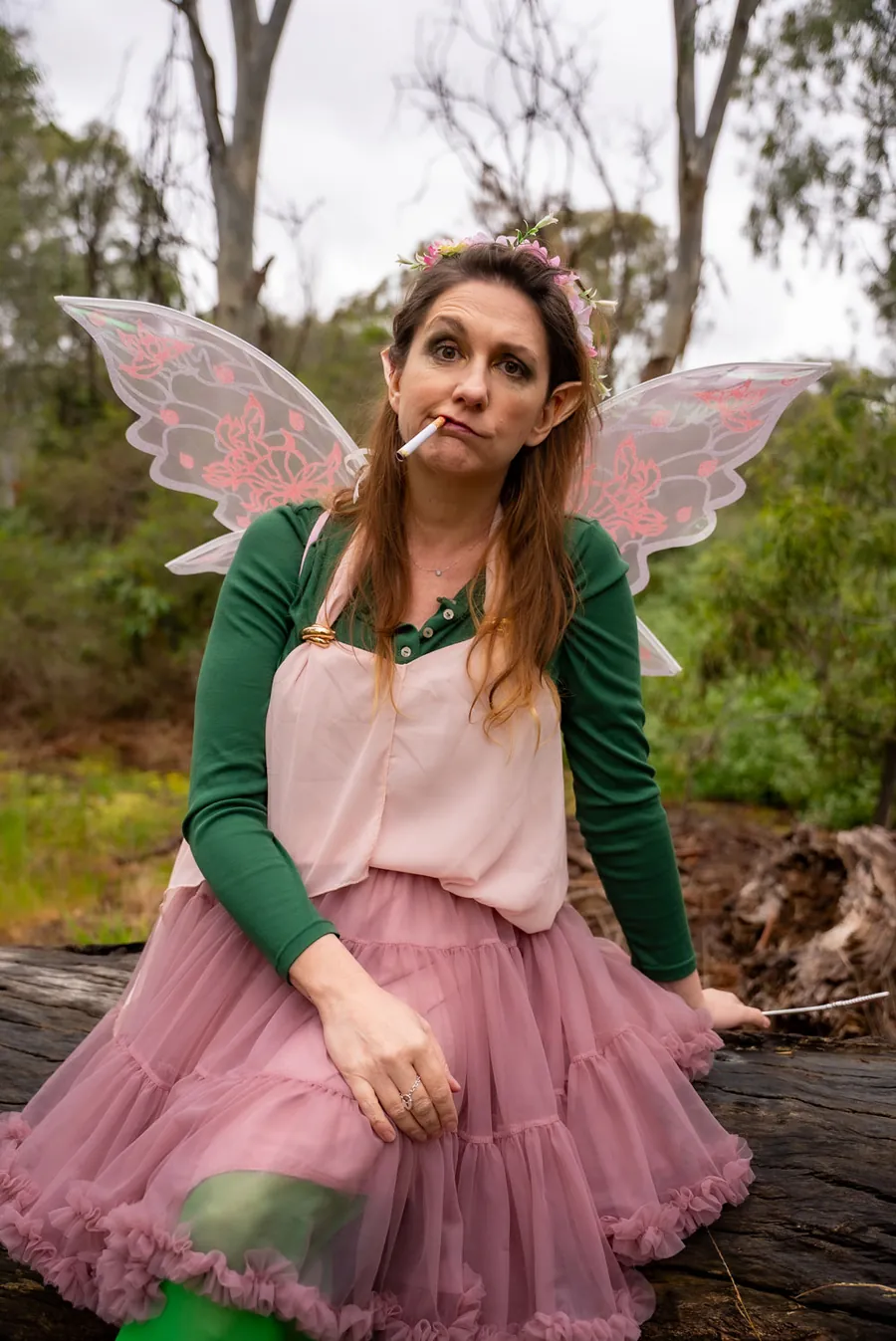 Thistle sitting on a fallen log in the bush in a pink tutu and green tights.
