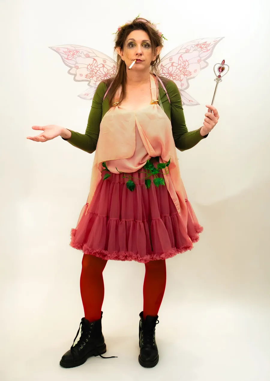 Full-length Thistle in pink tutu, red tights and black boots, shrugging with her wand in hand.